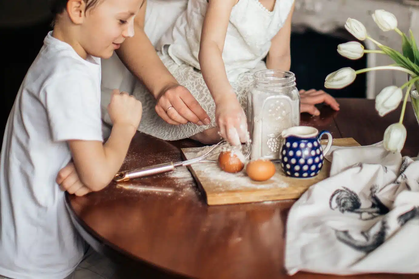 A child cooks with his mom, helping to crack eggs at a table showing cooking with kids